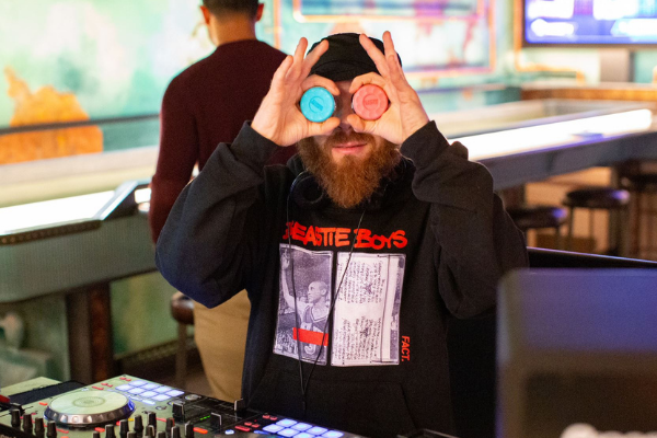 DJ playing music during brunch with shuffleboard pucks over his eyes.
