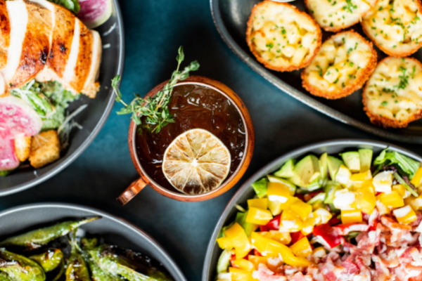Collection of menu items featuring the Notorious F.I.G mule, Chicken Caesar salad, the Rainbow Bowl, and Truffle Mac & Cheese Bites.