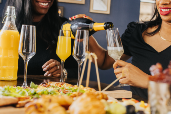 Two women pour glasses of bubbly for mimosas during brunch.